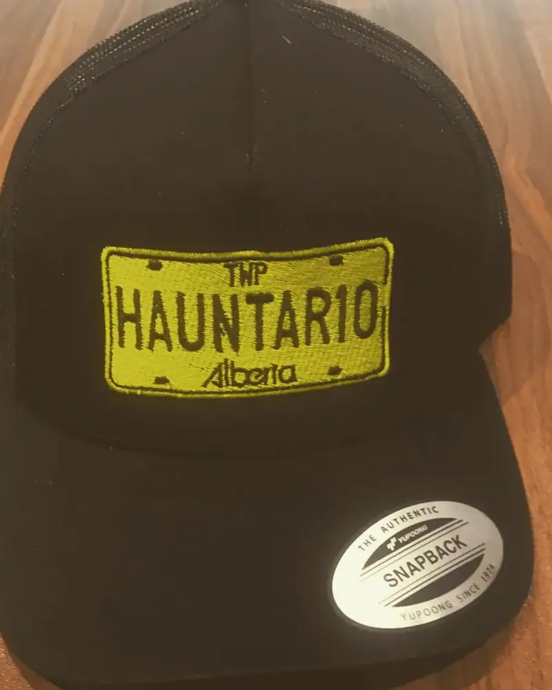 Black trucker snapback cap with a yellow HAUNTAR10 Alberta licence-plate patch